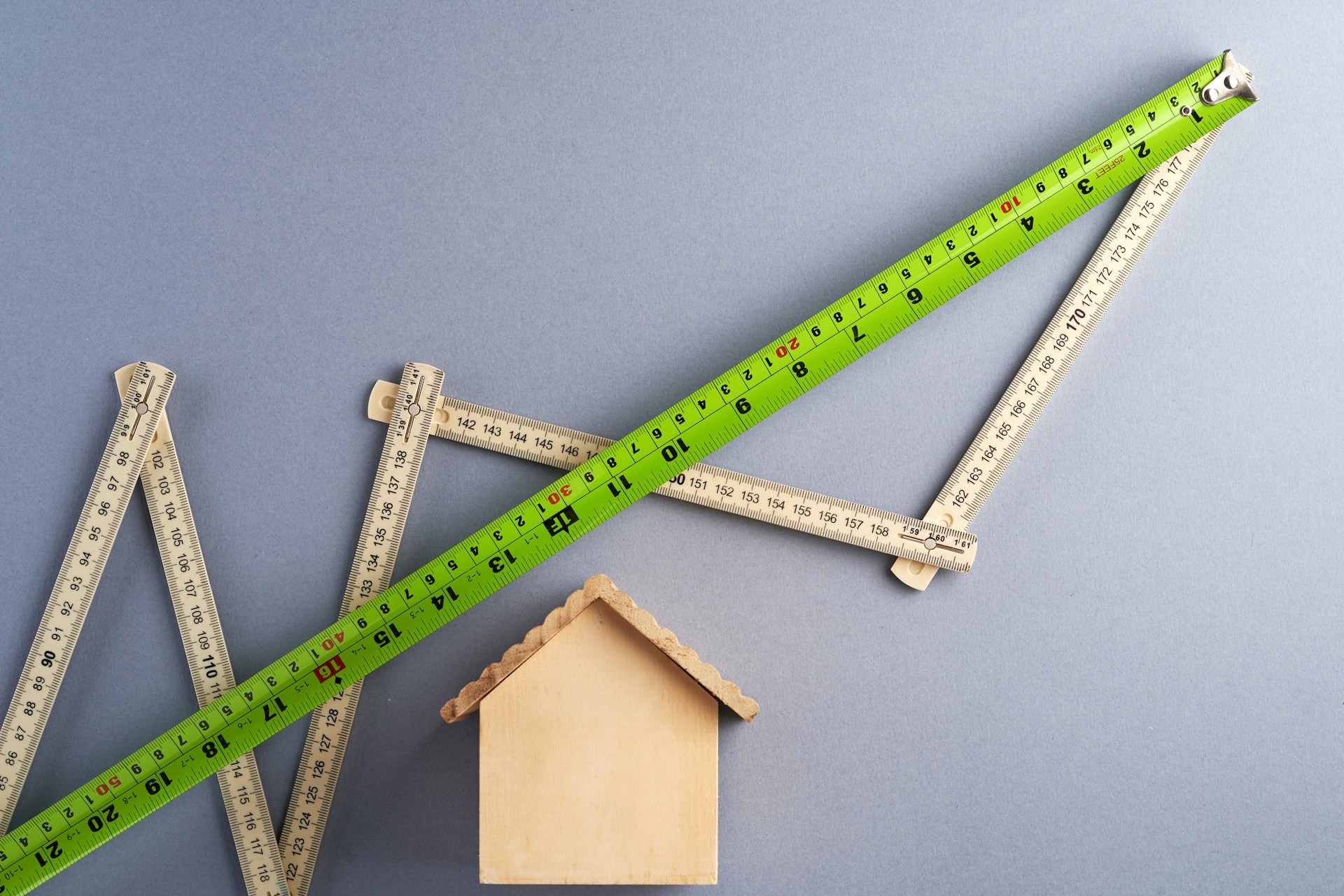 Zollstöcke bilden über einem Holzhaus eine steigende Kurve — Bauzinsen 2026 auf dem Weg nach oben